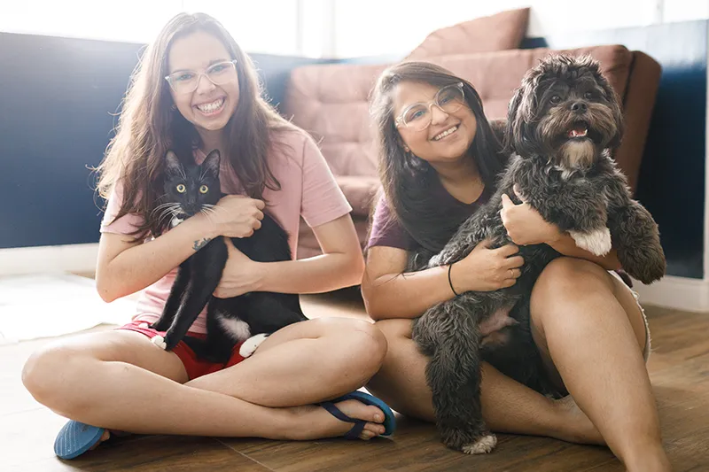 Two friends sitting together holding a dog and a cat